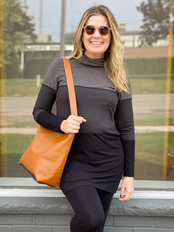 Woman standing in front of a window wearing Miik's Hasha colourblock twisted cowl tunic in grey stripe with black leggings.