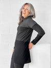 Woman standing in front of a wall wearing Miik's Hasha colourblock twisted cowl tunic in grey stripe and leggings.