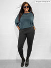 Woman standing in front of a white wall with hands in her pockets wearing Miik's Henley lounge jogger in charcoal with a long sleeve top in fog 