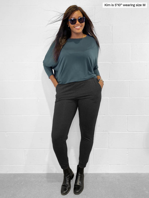 Woman standing in front of a white wall with hands in her pockets wearing Miik's Henley lounge jogger in charcoal with a long sleeve top in fog 