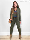 Woman standing in front of a white wall wearing a sage melange blazer and a striped tee along with Miik's Henley lounge jogger in sage melange
