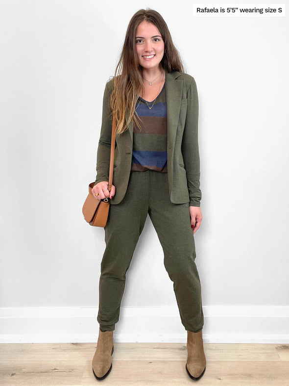Woman standing in front of a white wall wearing a sage melange blazer and a striped tee along with Miik's Henley lounge jogger in sage melange
