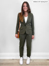 Woman standing in front of a white wall wearing Miik's Henley lounge jogger in sage melange with a matching colour blazer closer with a white tee