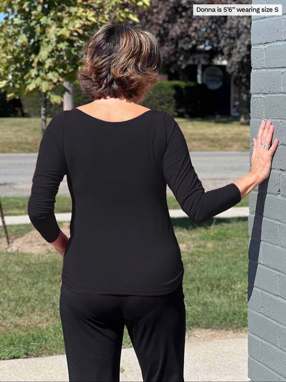 A woman standing outside with her back to the camera showing the back of the Hilden boatneck top in black.