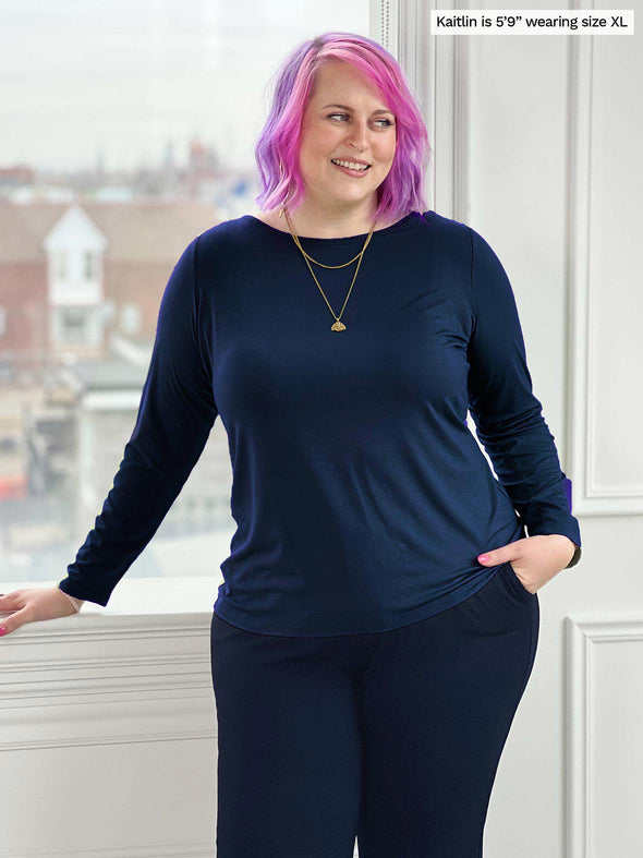 Woman standing in front of a window/white wall wearing Miik's Hilden ballet top in navy with a matching colour pant