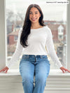 Woman sitting in front of a window smiling wearing Miik's Hilden ballet top in white with jeans