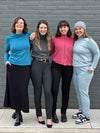 Group of women standing in front of a brick wall all wearing Miik's India reversible fleece funnel neck sweater in different colours: teal melange, granite, pomegranate and mist