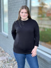 Woman standing next to a building wearing Miik's Jamie round neck long-sleeve in black with blue jeans.