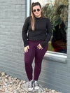 Woman standing next to a building wearing Miik's Jamie round neck long-sleeve in black with burgundy leggings.