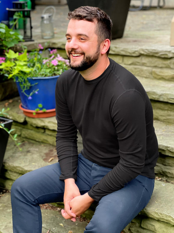 Man sitting on stairs outside wearing Miik's Jamie round neck long-sleeve in black with blue pants.