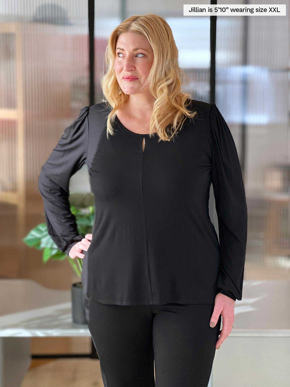 Woman standing in an office wearing Miik's Janette puff sleeve keyhole shirt in black with pants.