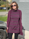 Woman smiling while standing in front of a building wearing Miik's Jordanna turtleneck tunic in port melange stripe with a long cardigan in port melange and black pant