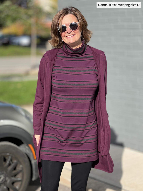 Woman smiling while standing in front of a building wearing Miik's Jordanna turtleneck tunic in port melange stripe with a long cardigan in port melange and black pant