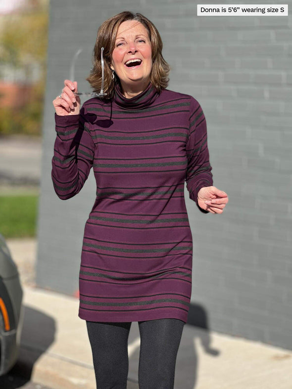 Woman smiling standing in front of a building wearing Miik's Jordanna turtleneck tunic in port melange stripe and charcoal legging