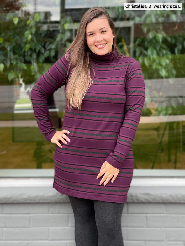Woman smiling while standing in front of a window wearing Miik's Jordanna turtleneck tunic in port melange stripe and charcoal legging