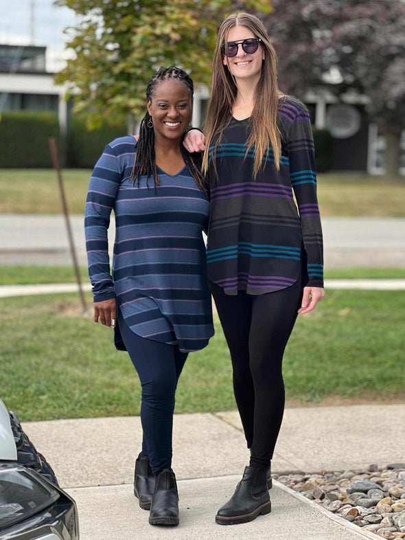 Two women smiling standing on a sidewalk wearing Miik's Juno reversible tunic, one in the navy jewel tone stripe and the other one in teal amethyst stripe print