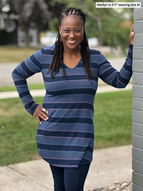 Woman smiling standing next to a brick wall wearing Miik's Juno reversible tunic in navy jewel tone stripe and navy leggings