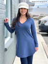 Woman standing next to a building wearing Miik's Juno reversible long sleeve tunic in navy melange with navy leggings and a white hat. 
