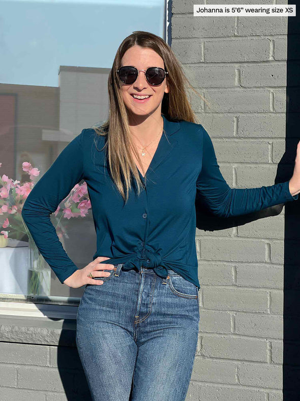 Woman smiling wearing Miik's Keeley notched collar long sleeve blouse knotted in teal with jeans and sunglasses  
