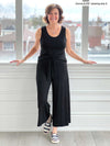 Miik founder Donna (five feet six, size small) smiling in front of a window wearing Miik's Kimmay open-back capri jumpsuit in black with nautical striped sneakers 