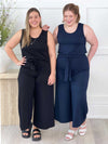 Miik model Christal (five feet three, size large) standing next to model Bri (five feet five, size extra large) both smiling and wearing Miik's Kimmay open-back capri jumpsuit in thw two colours available: black and navy