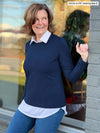 Woman leaning on a window wearing Miik's Langley faux crew neck collared shirt in navy with jeans.
