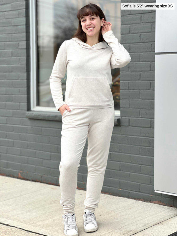 Woman smiling standing in front of a building wearing Miik's Linaya luxe fleece jogger in oatmeal melange with a matching colour cropped fleece hoodie