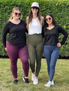 Three women smiling standing on grass wearing Miik's Lisa2 colourful high waisted legging in three different colours: port melange, sage melange and navy melange 