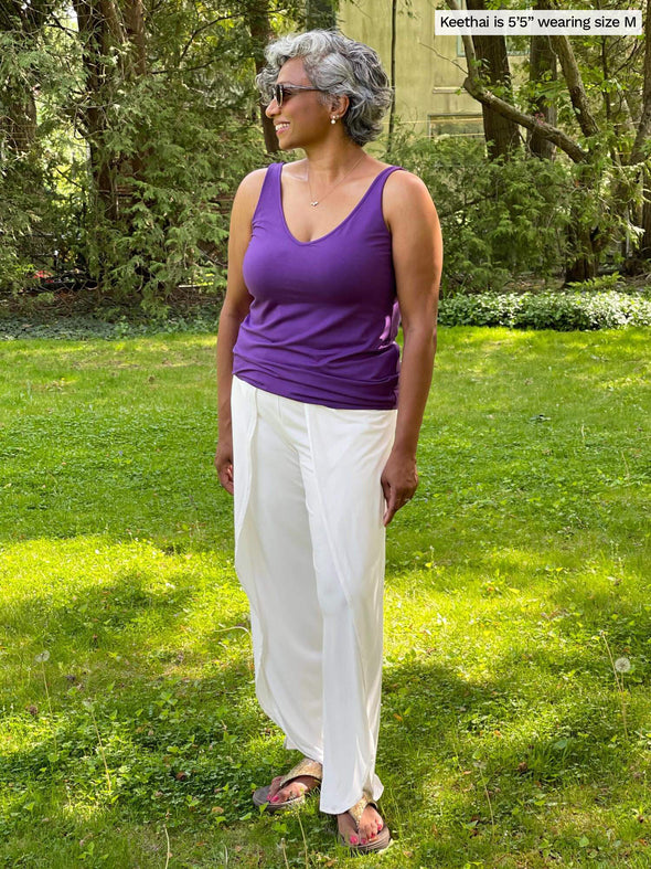Woman standing in a backyard looking away wearing a white pant with Miik's Lori reversible slouchy tank top in grape purple 