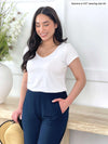 Miik model Yasmine (five feet tall, size extra small, petite) smiling while looking down wearing Miik's Marianna reversible classic tee in white with a navy pant