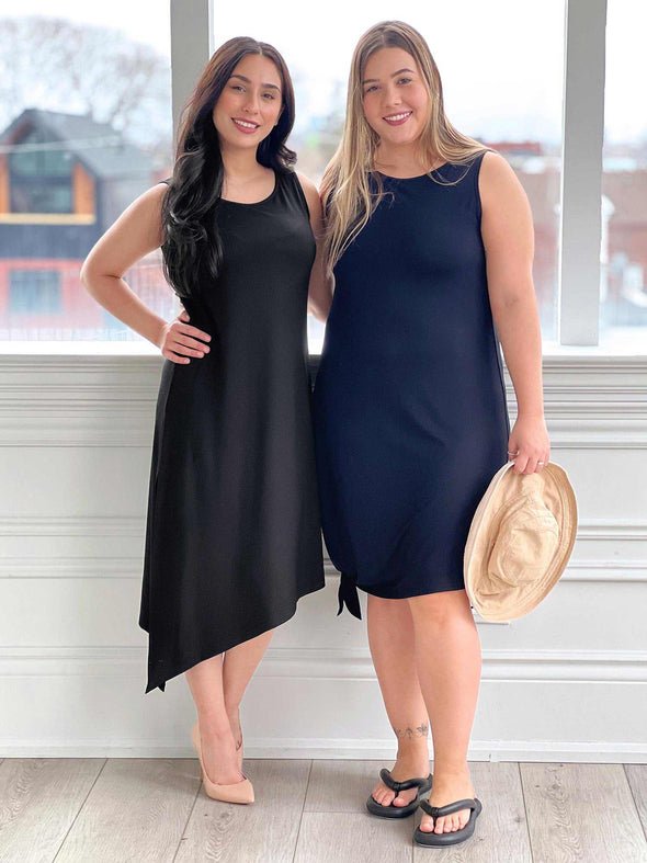 Two women standing next to each other in front of a window both wearing Miik's Mariska asymmetrical tunic dress, one in black dressed up with high heels and the other in navy dressed down with flip flops and tied 
