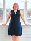 Woman smiling standing in front of a window wearing Miik's Mary Jo sleeveless v-neck dress in navy 