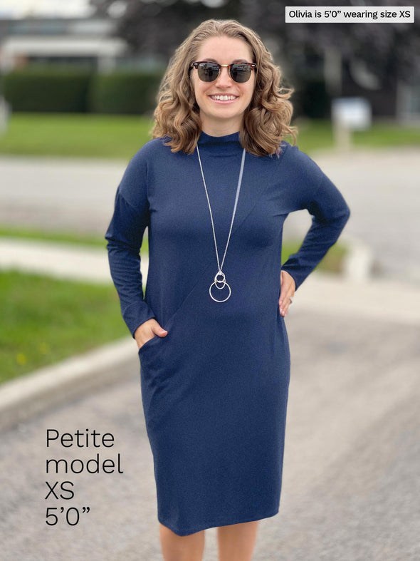 Woman smiling wearing Miik's Max mock neck pocket dress in navy melange with a long neckless and sunglasses