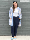 Woman smiling and standing in front of a brick wall wearing Miik's Melanie classic cardigan with pockets in denim peony stripe, white t-shirt and navy pants