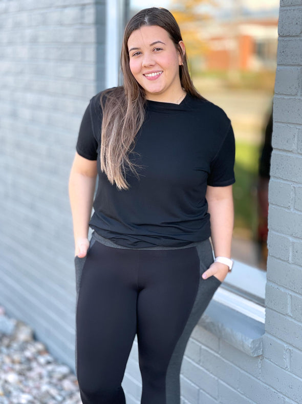 Woman standing in front of a window wearing Miik's Mick square neck t-shirt in black with pocket leggings.