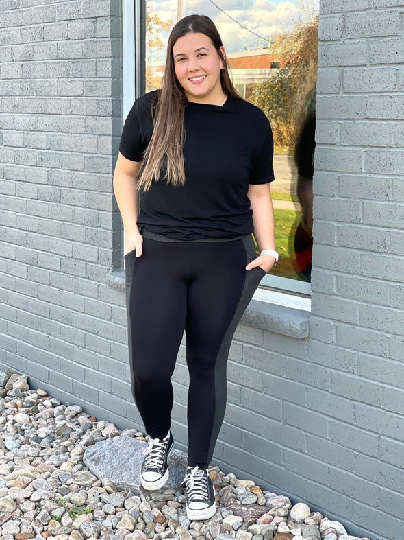 Woman standing in front of a window wearing Miik's Mick square neck t-shirt in black with pocket leggings.