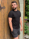 Man leaning on a door wearing Miik's Mick square neck t-shirt in black with grey shorts.