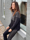 Woman sitting by the window wearing Miik's Oaklynn colour block cowl top in grey with matching leggings.