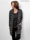 Woman looking away in front of a white wall wearing Miik's Paulina pocket hooded cardi in charcoal ompre stripe