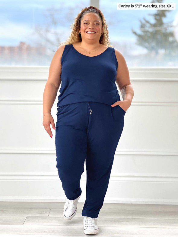 Miik model Carley (five feet two, size double extra large) smiling with hands on her pockets wearing Miik's Perle open-back sleeveless jumpsuit in navy