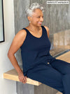 Woman smiling sitting next to a fireplace wearing Miik's Perle open-back sleeveless jumpsuit in navy