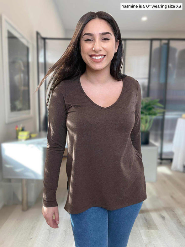 Woman standing in an office wearing Miik's Priya modern long sleeve v-neck top in brown with jeans.