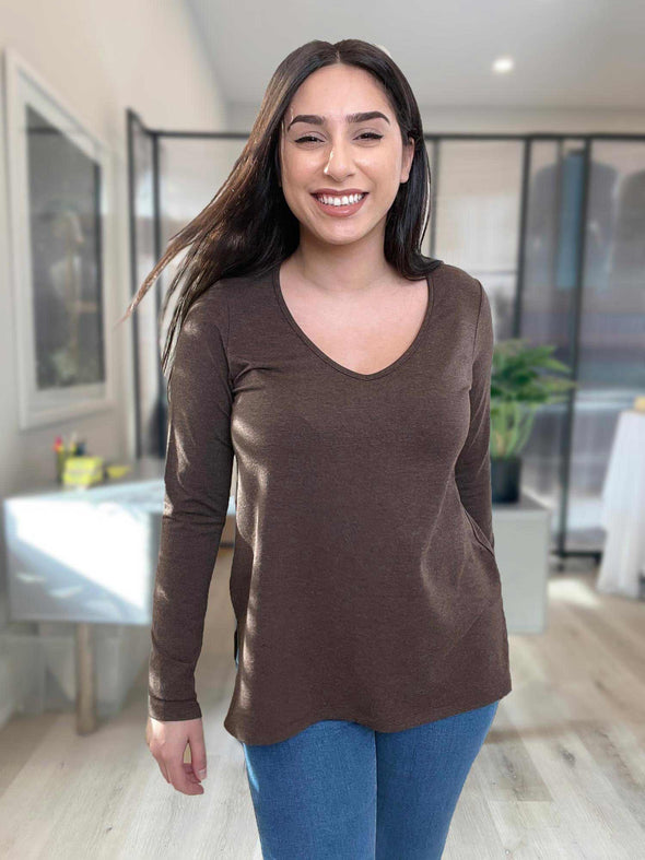 Woman standing in an office wearing Miik's Priya modern long sleeve v-neck top in brown with jeans.