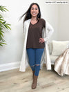 Woman standing wearing Miik's Priya modern long sleeve v-neck top in brown with jeans and an off white cardigan.