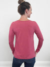 Woman standing with her back towards the camera wearing Miik's Priya modern long sleeve v-neck top in pink with jeans.