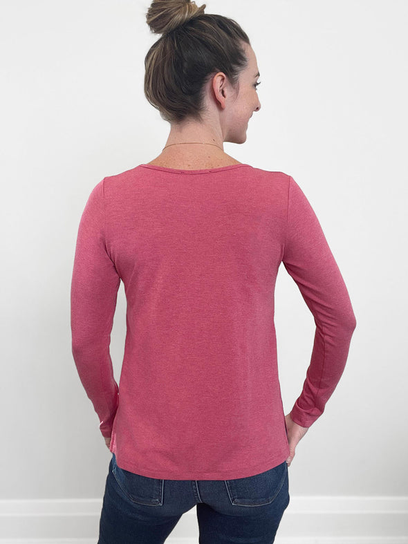 Woman standing with her back towards the camera wearing Miik's Priya modern long sleeve v-neck top in pink with jeans.