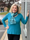 Woman standing next to a building wearing Miik's Priya modern long sleeve V-neck top in teal melange with black pants.