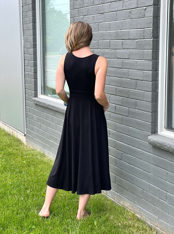 Miik model Johanna (five feet six, size xsmall) standing with her back towards the camera showing the back of Miik's RJ midi flounce dress with pockets in black 