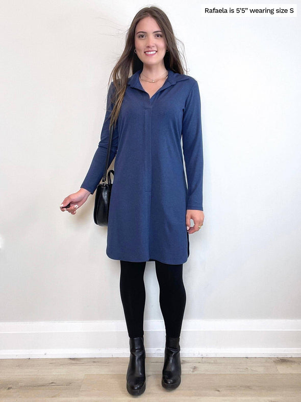 Woman standing in front of a white wall wearing Miik's Rafaela dressy collared tunic top in navy melange with black legging and boots