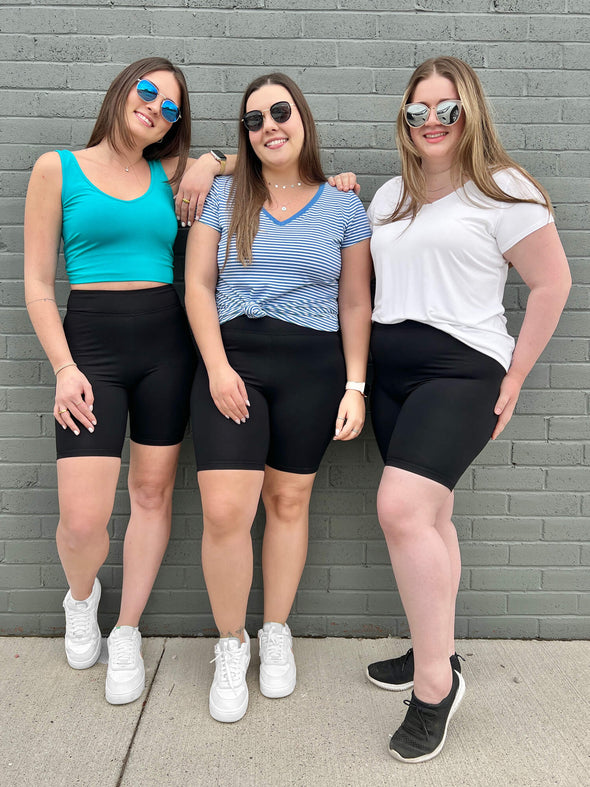Three women standing in front of a brick wall wearing Miik's Raven high waisted biker short in black  along with marianna t-shirt in white, stripped blue sutton and lori top in ocean